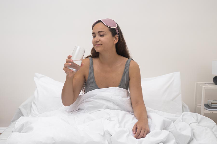 Se recuperando da Dengue, jovem deitada com mascara de dormir erguida para os cabelos, segurando um copo de agua