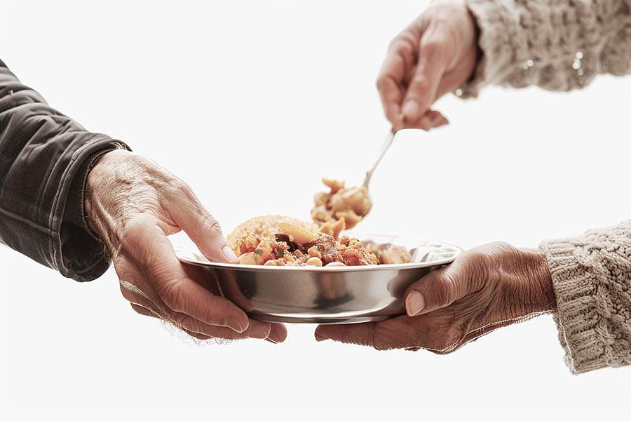 prato com mix de frutas. Mãos de idosos dão suporte ao prato. Do lado feminino a senhora serve uma colherada. Alimentação para prevenção à demência