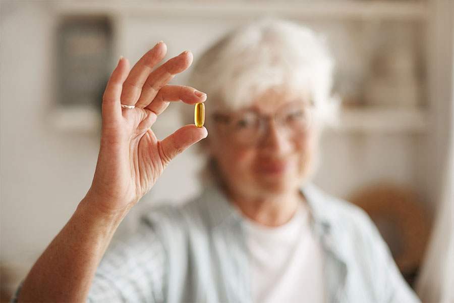 Senhora desfocada no fundo seguarado capsula de gel em primeiro plano em close representando Suplementos na Prevenção da Demência